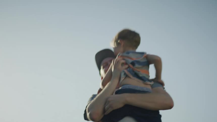 A boy runs through a field to his father who lifts him and playfully tosses him into the air