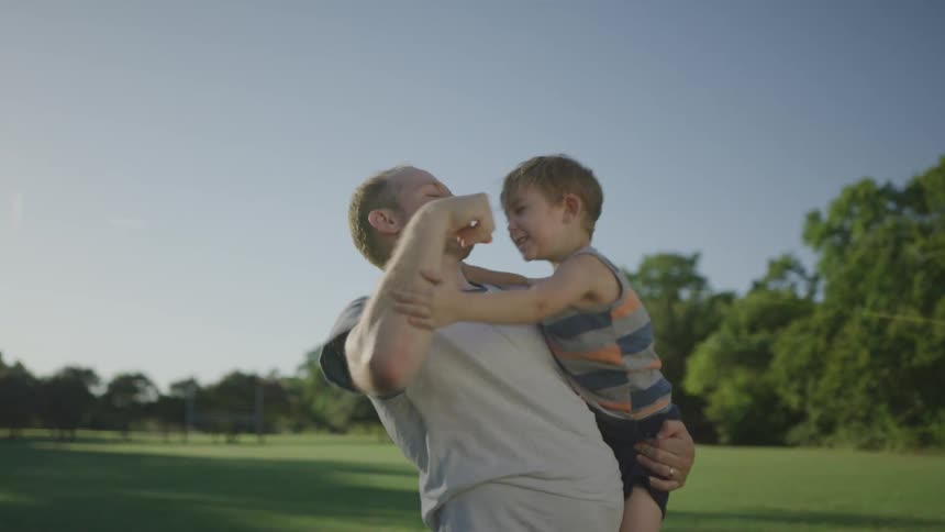 A dad tosses his son up in the air then tickles and kisses him at the park