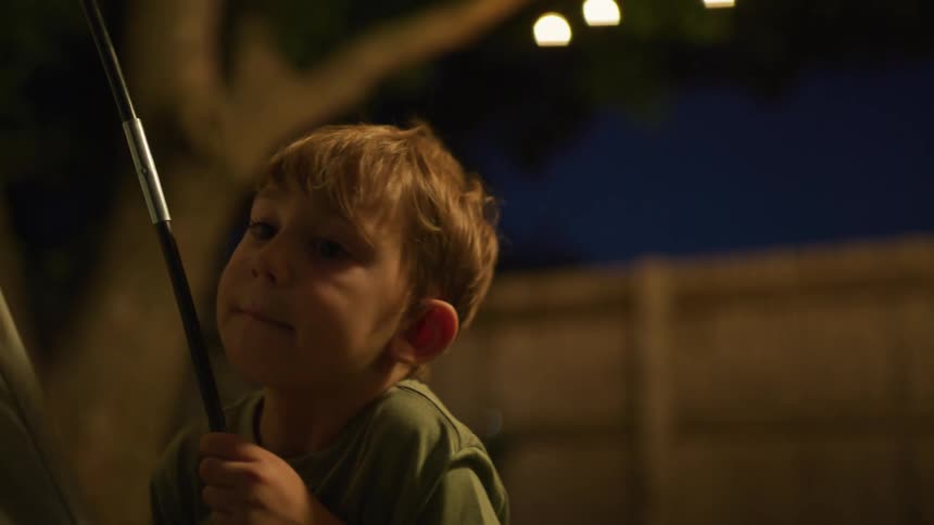 A young boy holds a rod outside at night