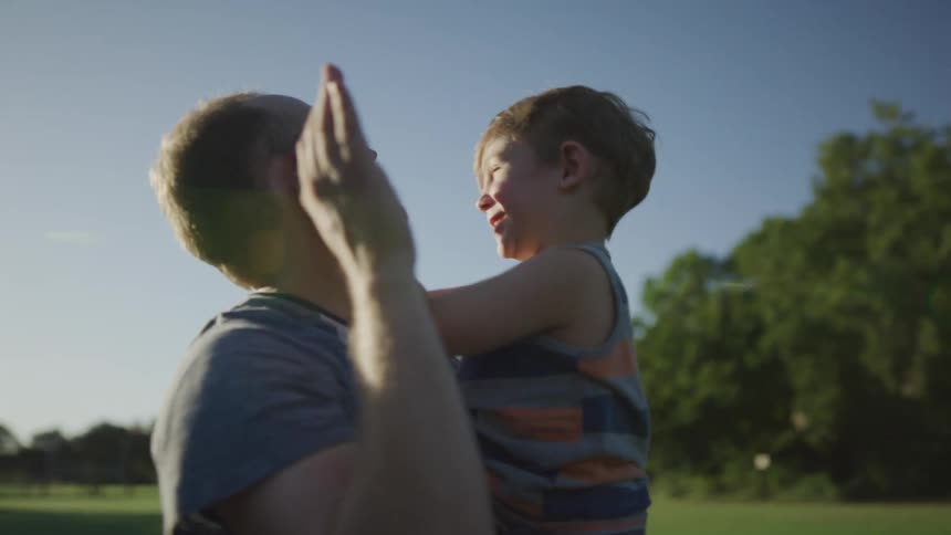 A dad tosses his son up in the air at the park as they laugh and play together