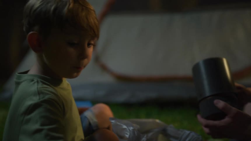 A man and his son unpack food during a camping trip as they sit outside their tent at night