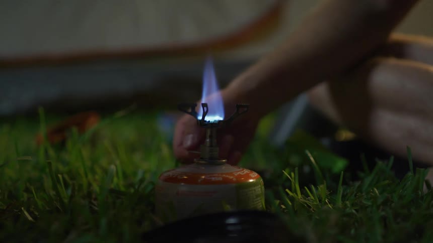 A person sitting on grass adjusting a torch with a flame