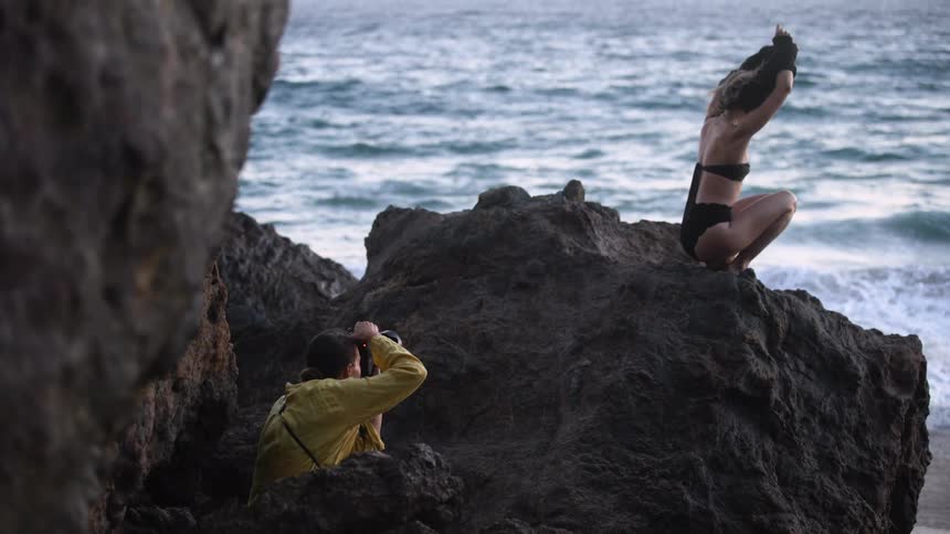 A photographer taking pictures of a woman in a bikini on a beach