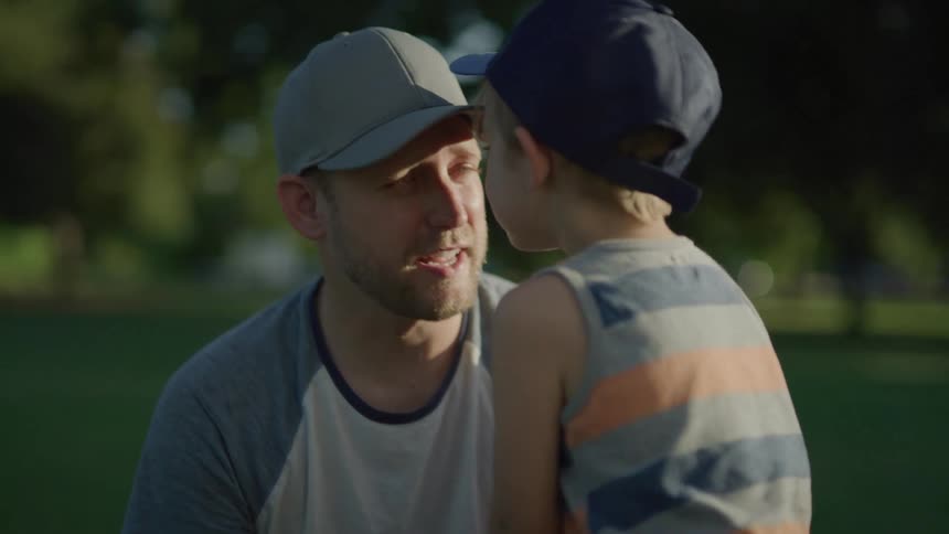 A father teaching his young son how to play baseball outside on a summer day