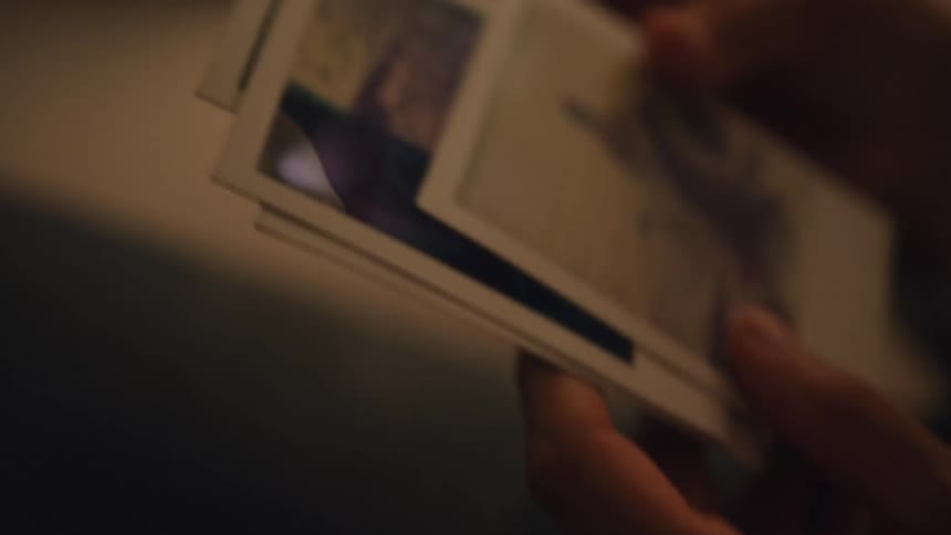 Woman standing on a dimly lit room looking at polaroid pictures
