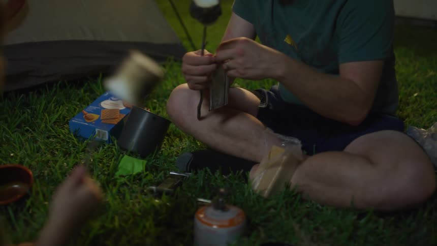 A boy and a man sitting on grass with toasted marshmallows on a stick