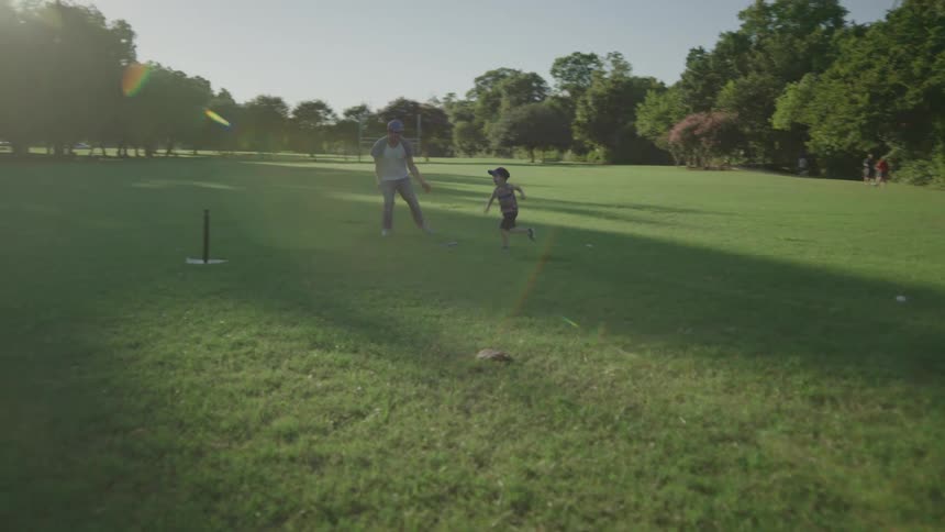 A man chases his young boy around while playing t ball at a park