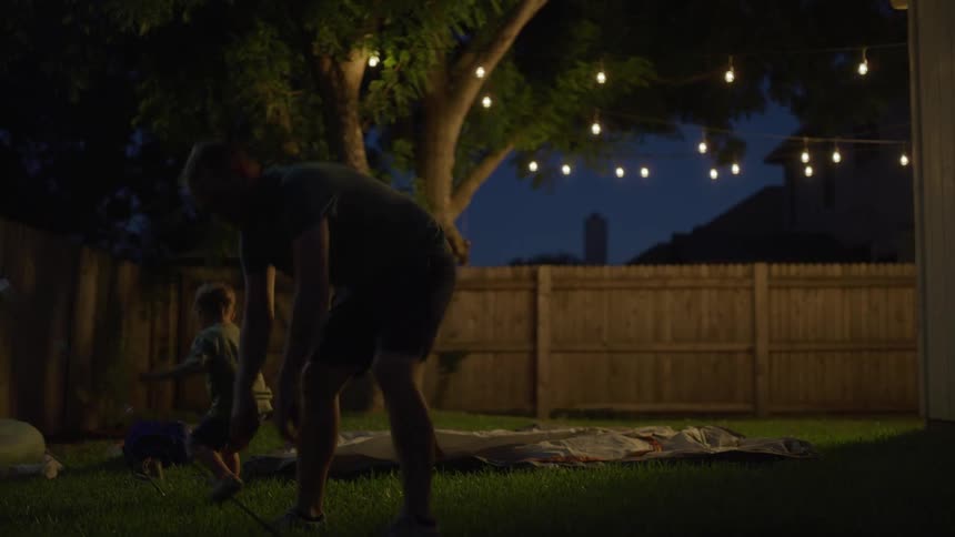 A man and a boy pitching a tent in the backyard with houses the sky and clouds in the background