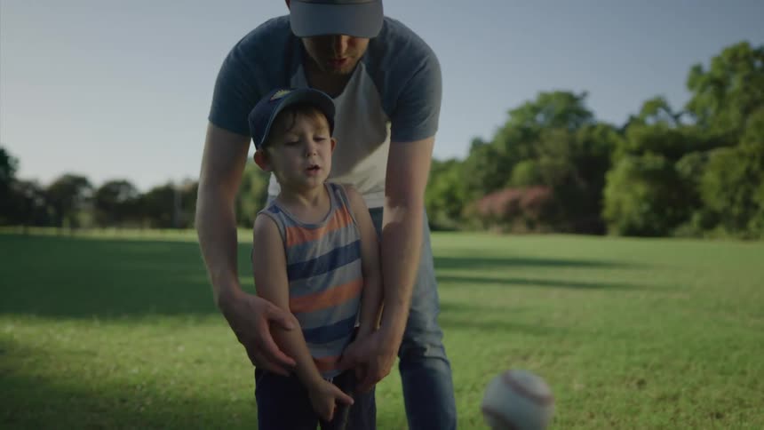 Father helps son with baseball practice on the park in the morning