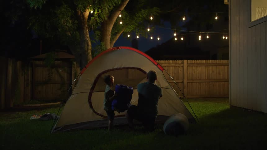 A man and boy set up sleeping bags in a backyard tent