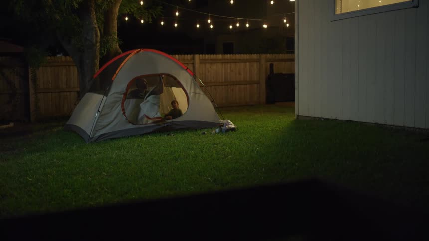 Father and son camping on a tent on the backyard at night