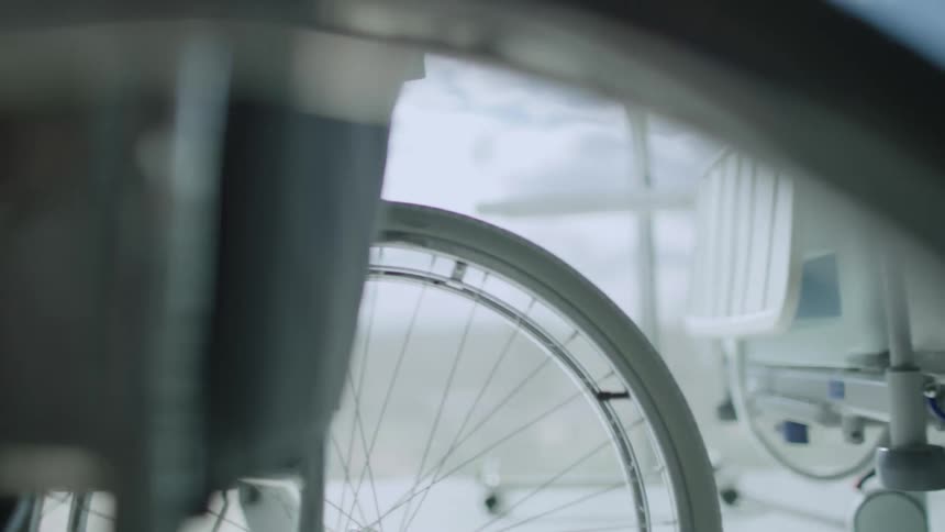 A person on a wheelchair in a room with a bed a chair and a window in the background