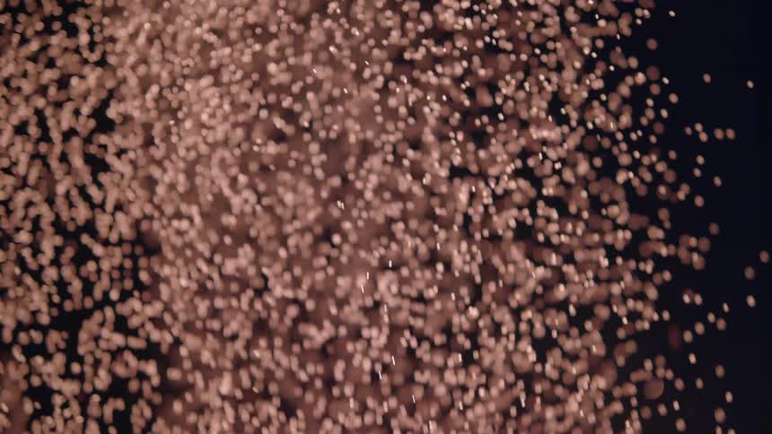 Numerous small white spheres spill down in darkness