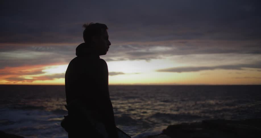 Silhouette of a young man standing in front of the ocean at sunset