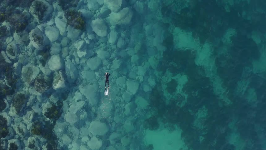 A scuba diver in a wetsuit swimming in turquoise ocean water