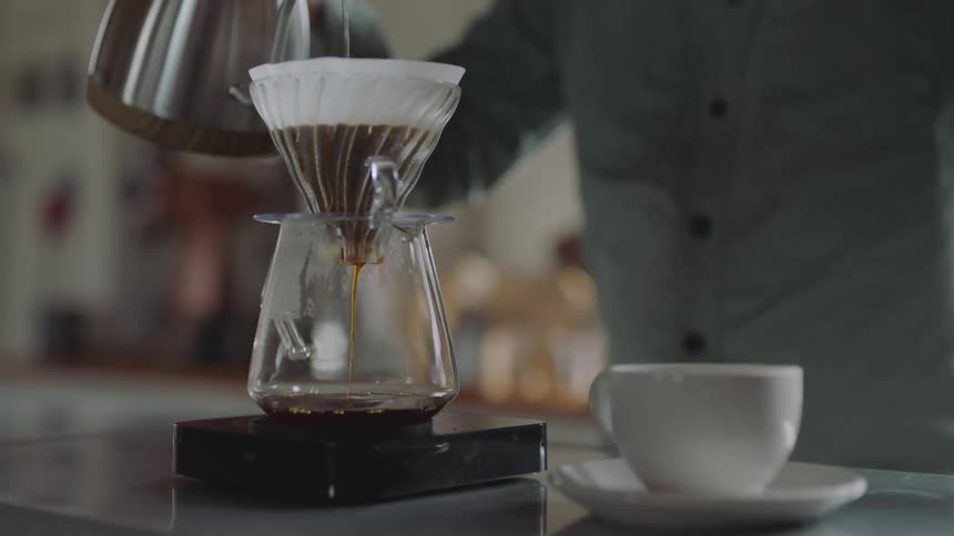 A person pours water into a coffee filter of coffee grounds and the coffee seeps through to a glass container