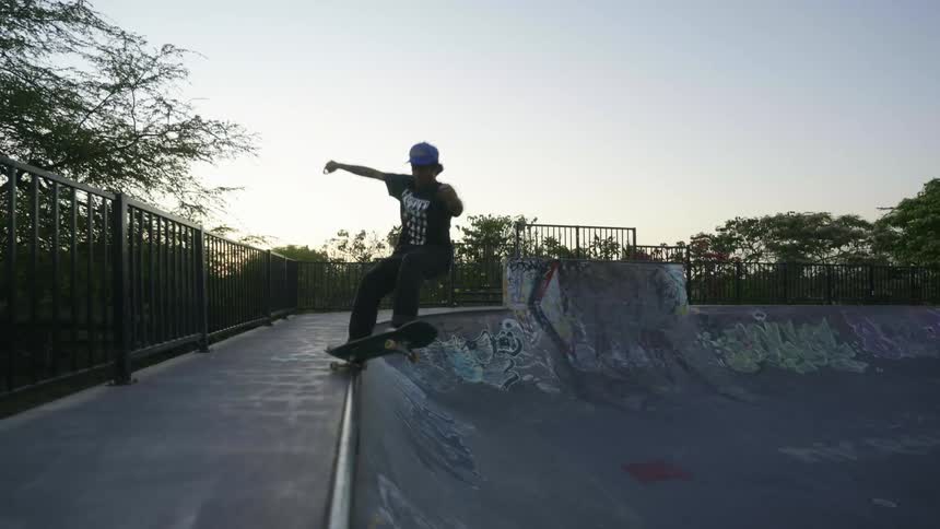 A skateboarder skates up a the edge of skating bowl and grinds on the edge before skating back down