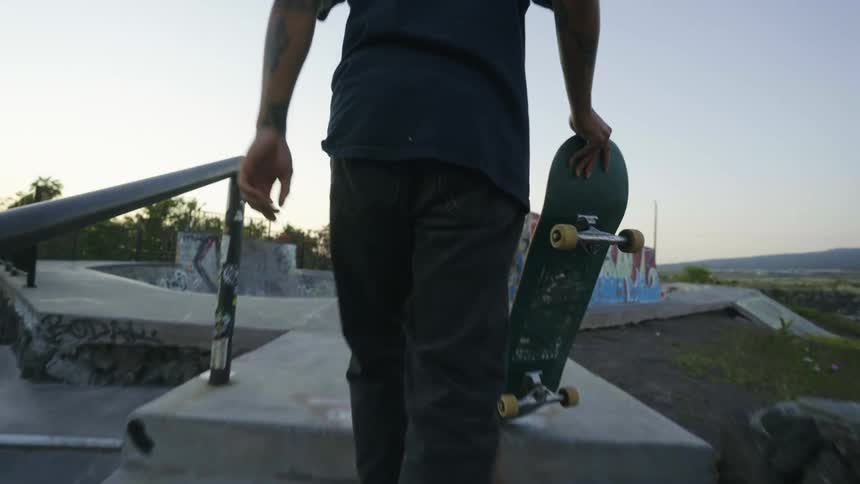 A man carries a skateboard up a set of cement stairs towards a skatepark