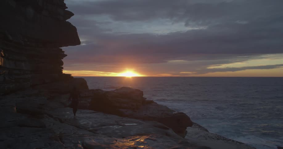 A person is walking by the coast at dusk