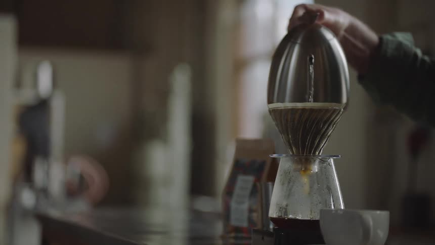 A man pours hot water through a coffee filter from a steaming kettle