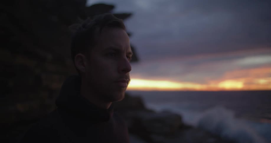 A man stands next to an ocean coast with a concerned look