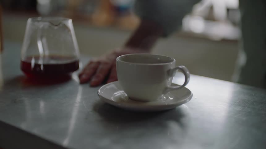 A cup of steaming hot coffee sitting on a countertop next to a glass carafe
