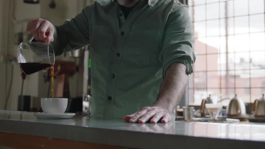 A man pours coffee from a small pitcher into a small mug