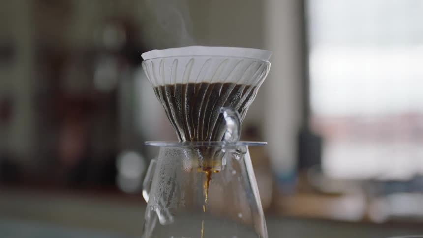 Coffee drips through a coffee filter into a glass coffee pot in a home kitchen during the day
