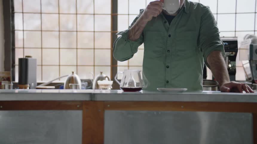 A man drinks coffee from a mug while standing in a kitchen during the day