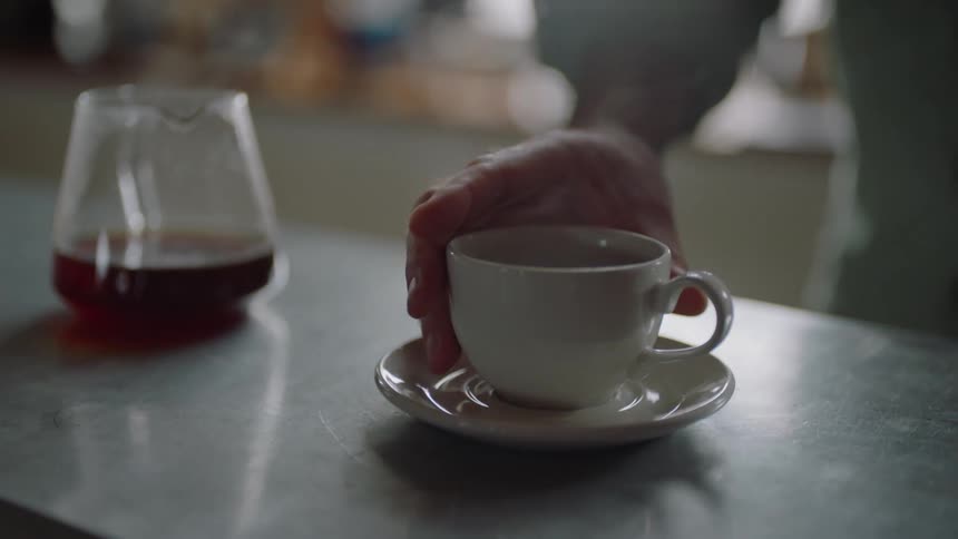 A man stops drumming his fingers on the counter and picks up a coffee cup