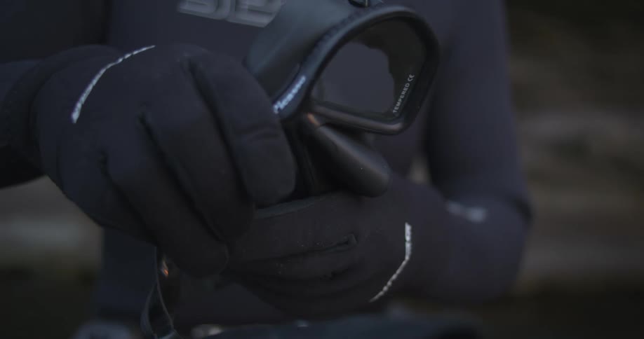 Snorkeler wearing gloves and a wet suit checks a snorkel and diving mask
