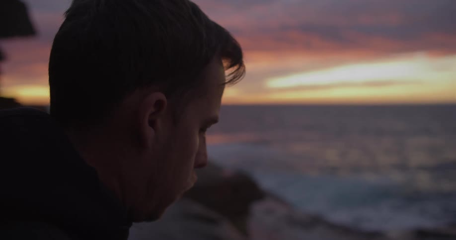 A man sitting next to the ocean looking at the sunset