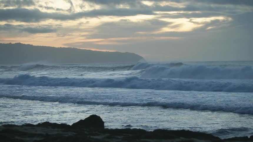 Two swimmers swim in the ocean waves under a cloudy sky