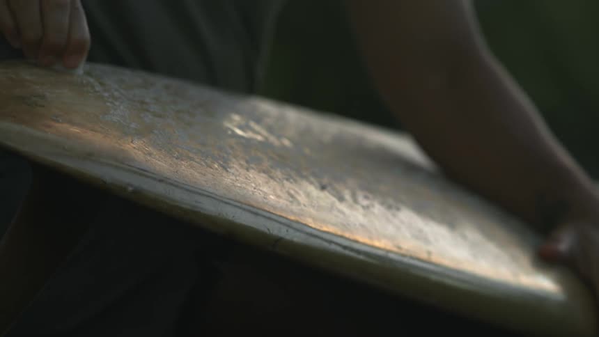 A person is rubbing a wax cube on a large piece of metal