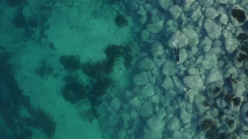 A person with a wetsuit and flippers swimming in a body of water with rocks