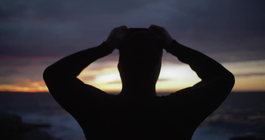 A man puts his hood on as he stands on the coast looking out over the water
