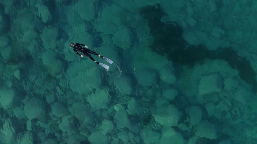 A person with a wetsuit and flippers swimming in a body of water with rocks