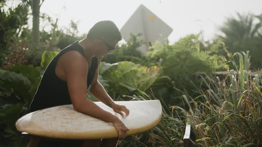 A man waxing a surfboard outside on a sunny summer day