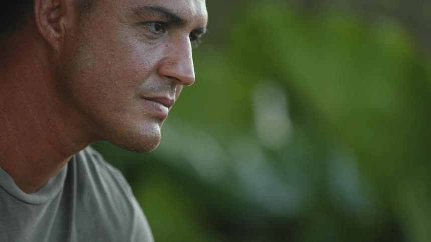 Man with a gold chain around his neck raises his head while outdoors