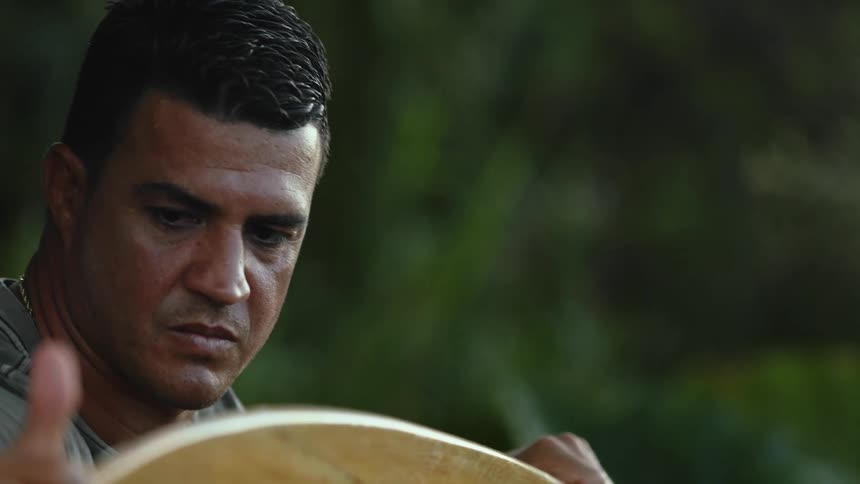 A man rubbing his hand along a surfboard outside