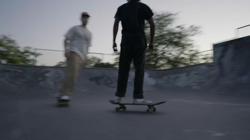 Two teenagers ride their skateboards back and forth in a graffitied skatepark
