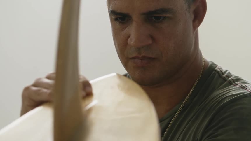 A man closely examines a wood surfboard