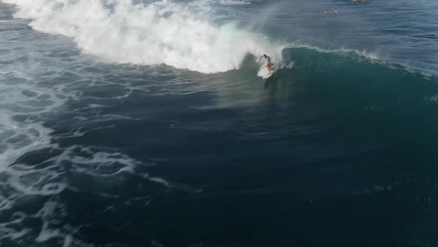 A surfer catches a large swell and rides the wave almost to the beach