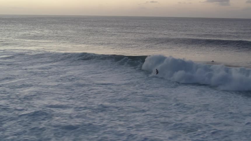 Large waves roll towards the shore while surfers try to ride them