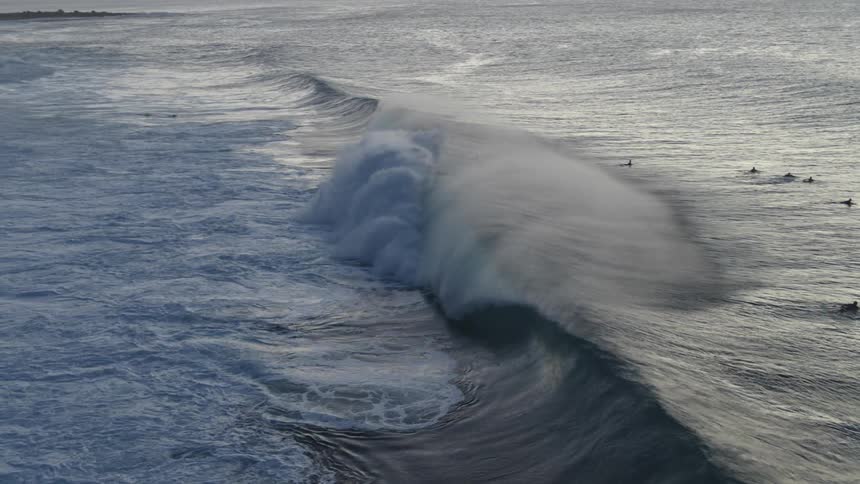 Surfers paddle out through a curling breaking wave