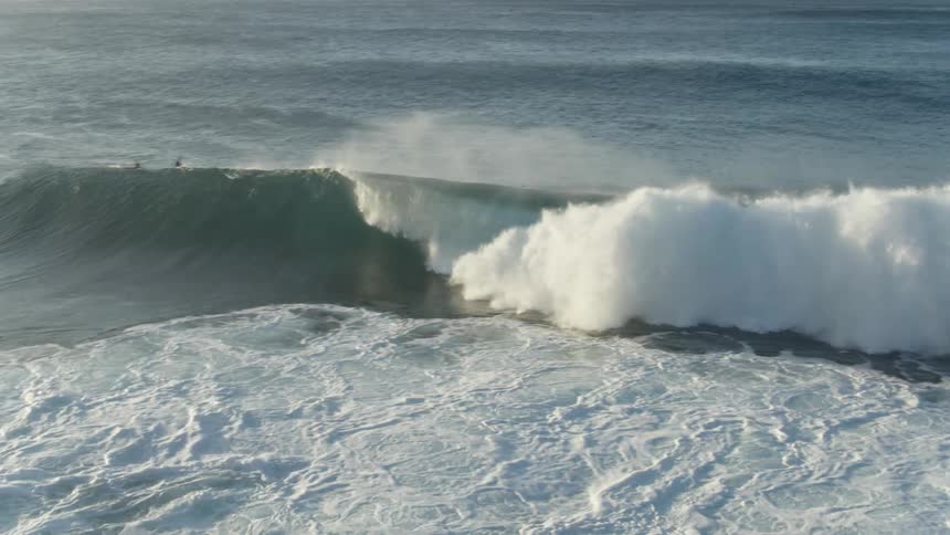 A man rides a large wave while others watch