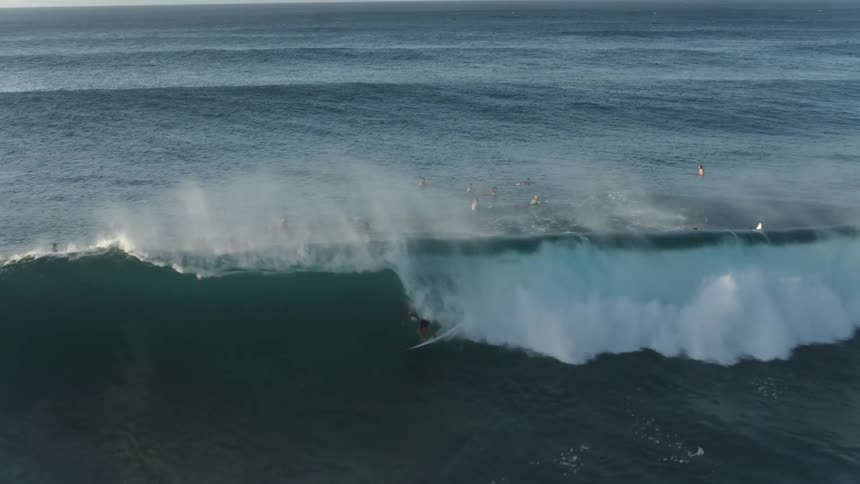 Surfers ride a curling breaking wave