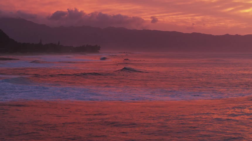 Waves roll in under a colorful red sky with the colors reflecting on the water