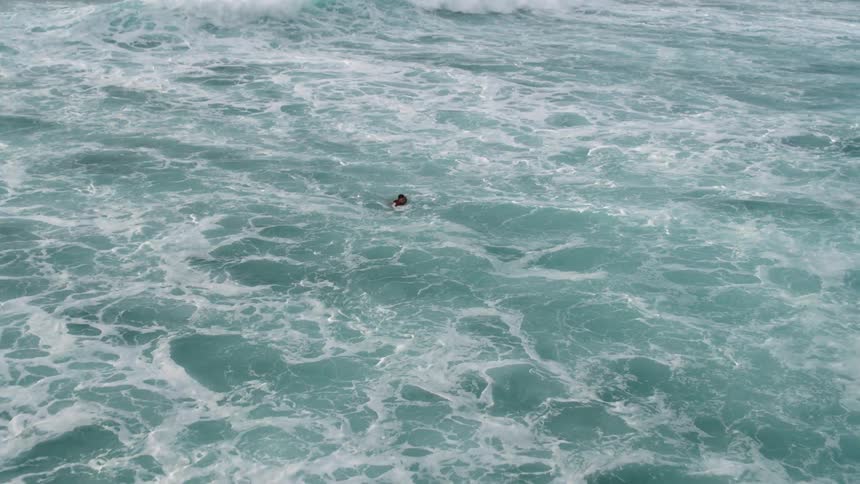 A surfer swims towards shore after breaking his board in powerful surf