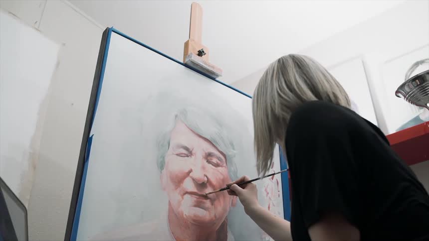 Woman painting a portrait of an older woman in her studio